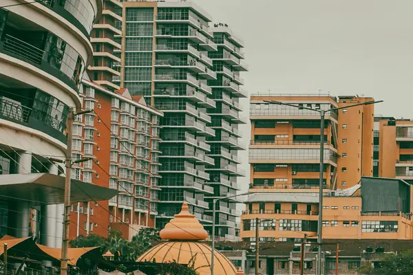 Curved balconies, a red-brick apartment block, a glass tower and an ochre dome on an overcast day