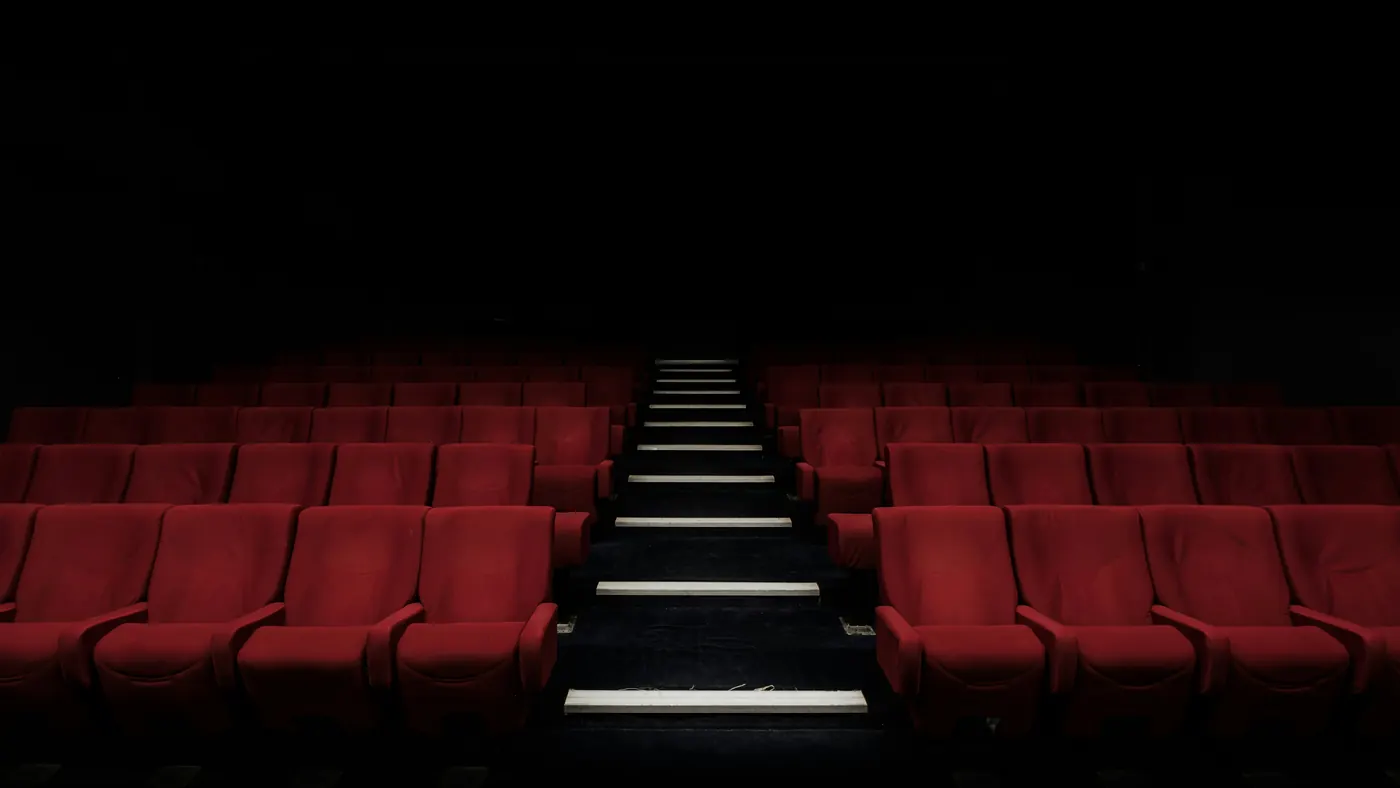 Rows of empty red cinema seats either side of softly lit steps in a dark auditorium