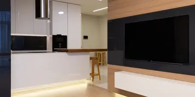 An open-plan apartment with a white kitchen, wooden bar stools and a wood-panelled wall with a large television (example photo, not of this place)