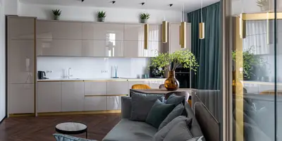 A grey velvet sofa in front of a long beige kitchen with brass pendant lights and a vase of green branches (example photo, not of this place)