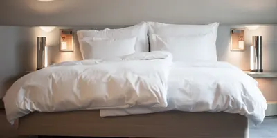 A large bed with crisp white linen between two softly lit bedside lamps (example photo, not of this place)