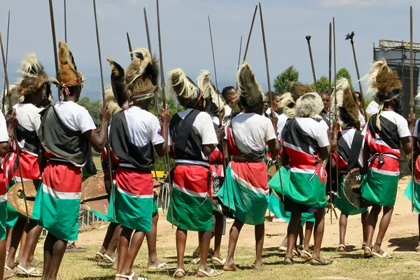 Dancers in headdresses and skirts in the colours of the Kenyan flag, holding spears