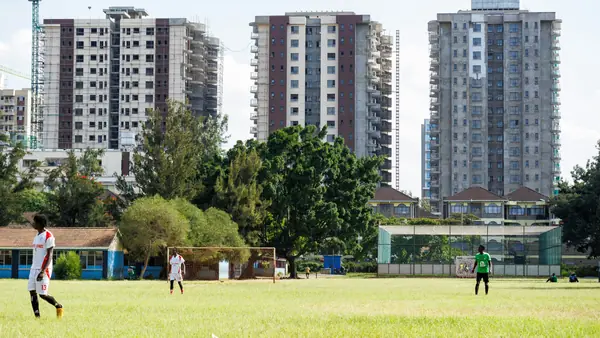 Players on a grass football pitch in front of new apartment towers