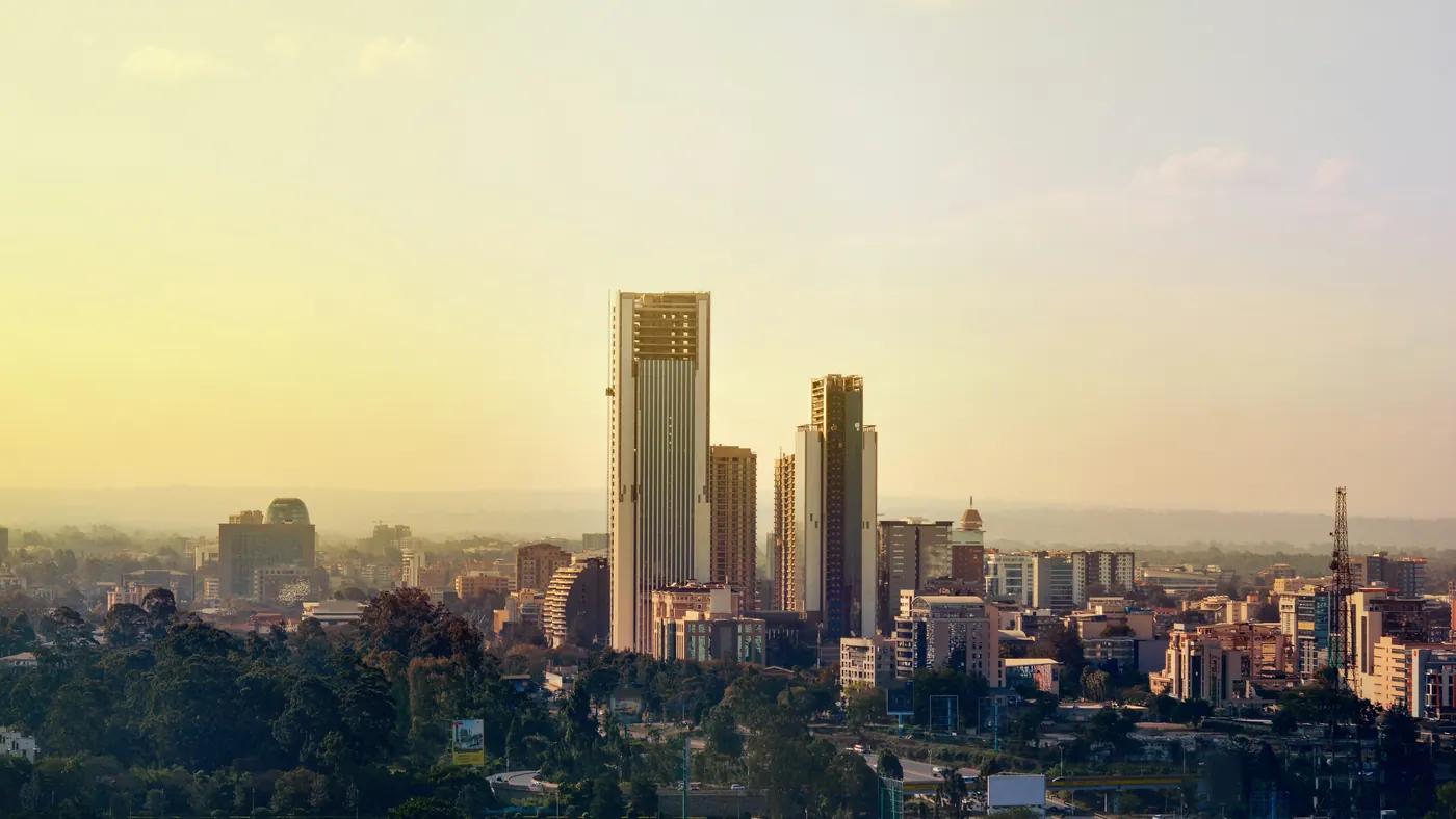 Nairobi skyline at golden hour, tall towers rising above a band of green trees
