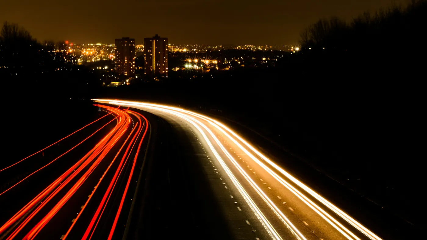 Long-exposure light trails of traffic curving along a highway towards a city at night