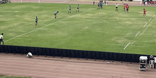 Players spread out across a grass pitch during a match, with the running track in the foreground