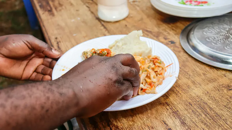 Hands eating from a plate of ugali and a vegetable stew on a weathered wooden table