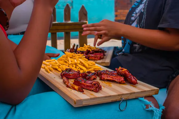 Glazed ribs and fries on a wooden board shared between friends outdoors