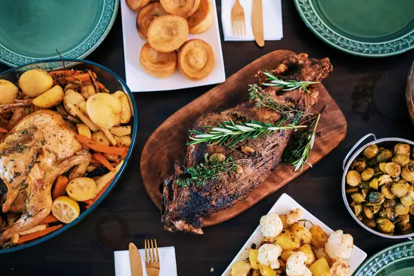A roast with rosemary on a board, surrounded by roast chicken, potatoes and vegetables
