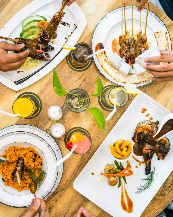 Overhead view of a round table with skewers, grilled chicken, rice and colourful drinks