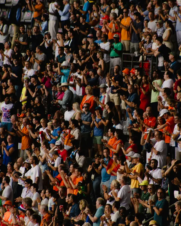A packed stadium stand of fans clapping and cheering
