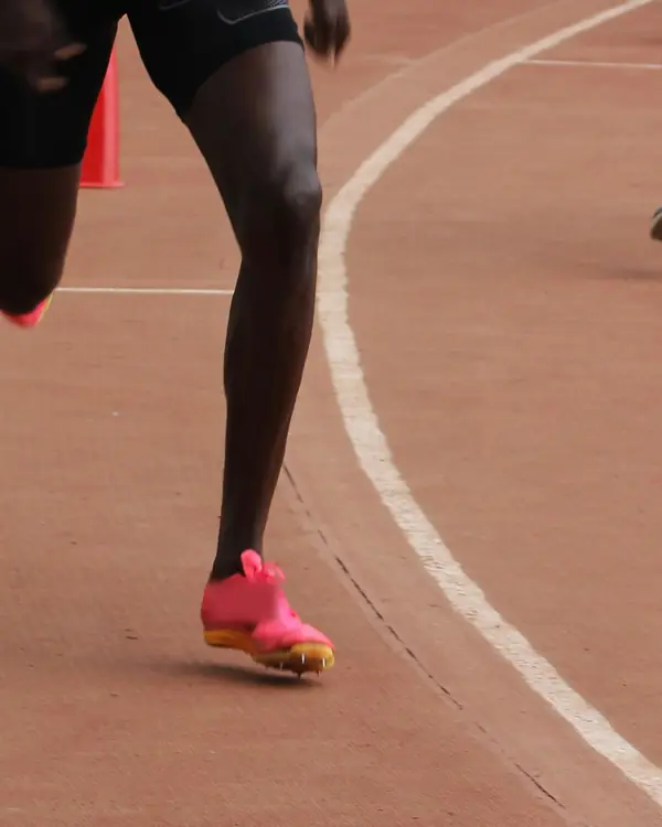 A sprinter's legs and pink spikes driving round the bend of a red running track