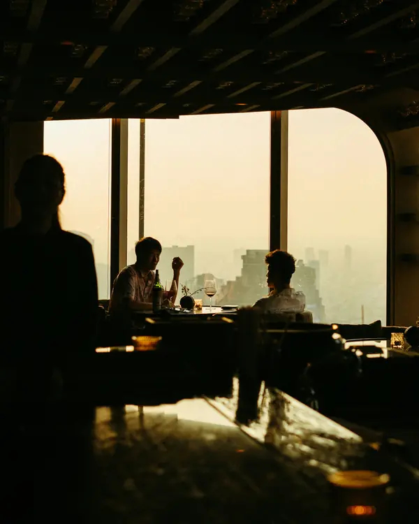 Two diners silhouetted at a window table high above a hazy city
